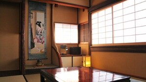 Ein traditioneller japanischer Raum mit Tatami-Boden, einem niedrigen Tisch, einem Fernseher und einer Schiebetür.