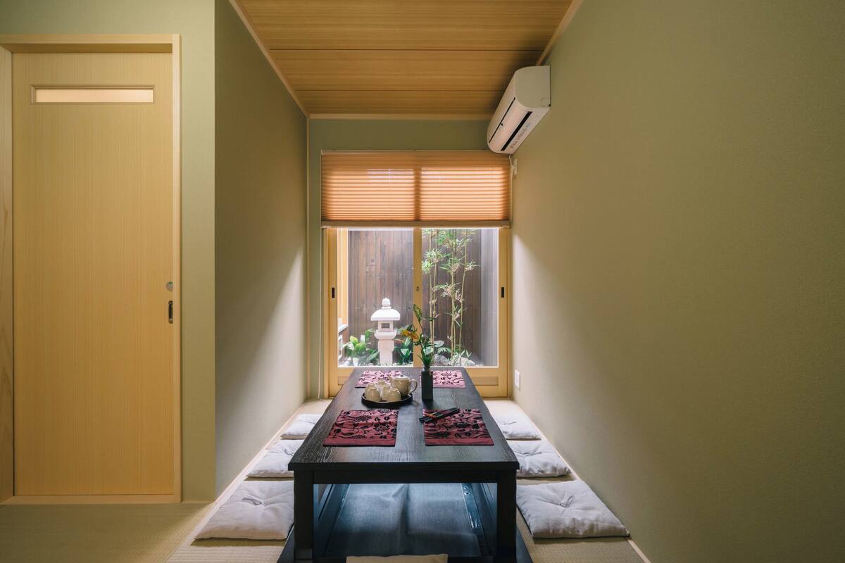A traditional Japanese room with tatami flooring, a low table with a tea set, and a view of a garden through a sliding door.