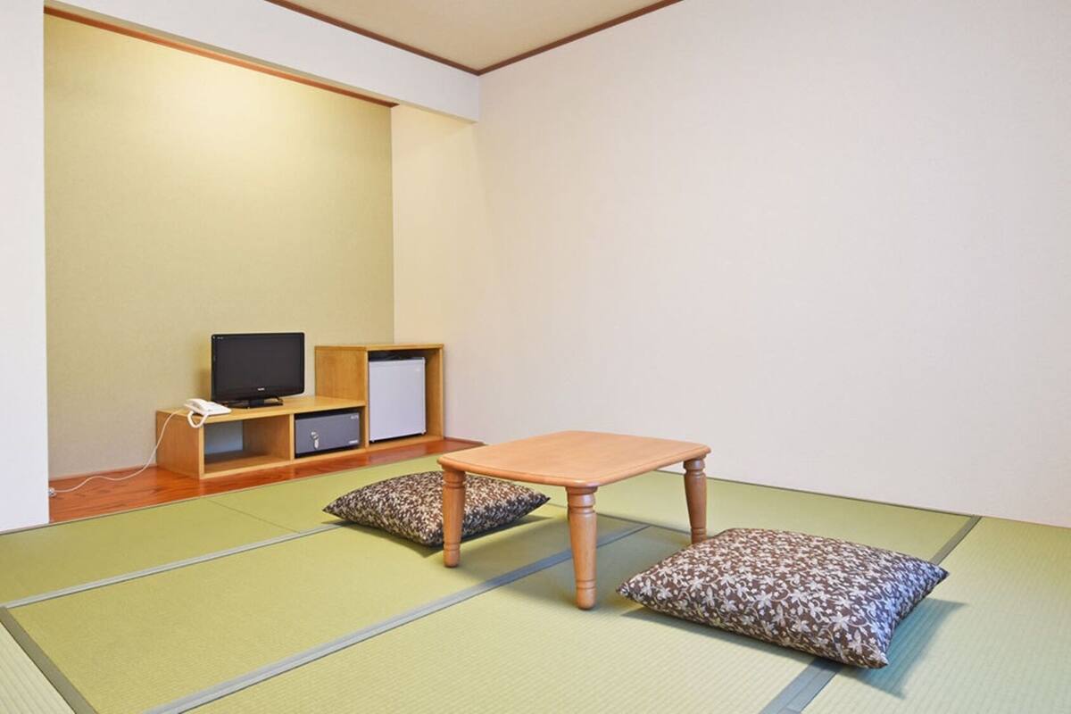 Una habitación con suelo de tatami, una mesa de madera baja, cojines, un televisor y un mueble pequeño.