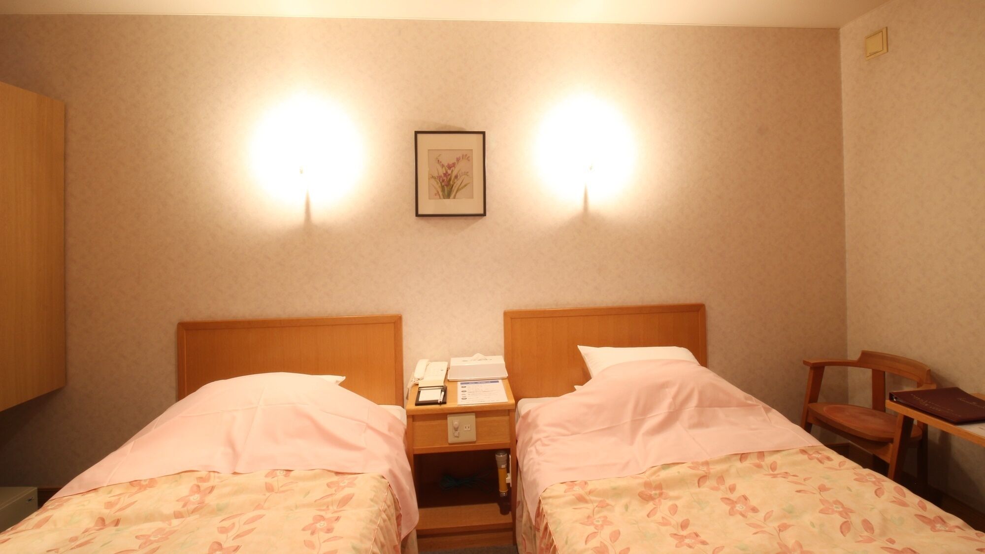 Habitación de hotel con dos camas, una mesita de noche con un teléfono y una lámpara, un cuadro en la pared y una silla.