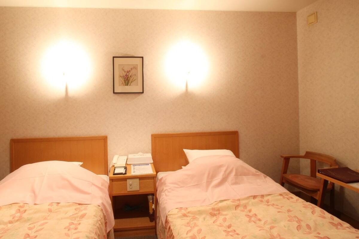 Habitación de hotel con dos camas, una mesita de noche con un teléfono y una lámpara, un cuadro en la pared y una silla.