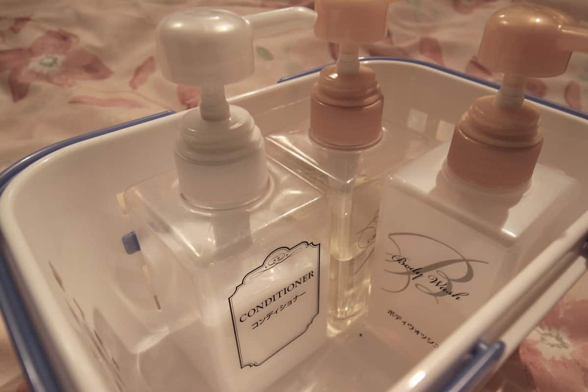 Een transparante plastic bak met drie flessen, waarvan er één 'CONDITIONER' bevat en een andere voorzien is van een handtekening.