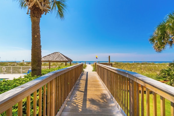 A wooden boardwalk leading to a beach with a palm tree and a gazebo. - Moonraker #5 - Charming 1/1, Sea South Properties - Charming 1bed/1bath condo (Gulf Shores)