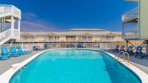 Un'area piscina con sedie blu, una piscina cristallina e una fila di edifici con balconi.