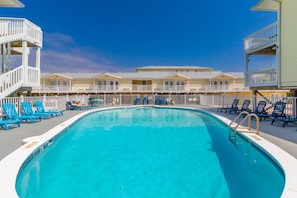A pool area with blue chairs, a clear blue pool, and a row of buildings with balconies. - Moonraker #5 - Charming 1/1, Sea South Properties - Charming 1bed/1bath condo (Gulf Shores)