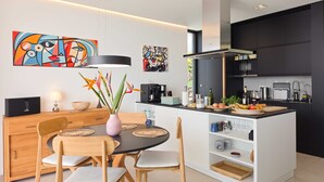 Een moderne keuken met een eethoek, met een centraal kookeiland, zwarte kasten en abstracte kunst aan de wanden.