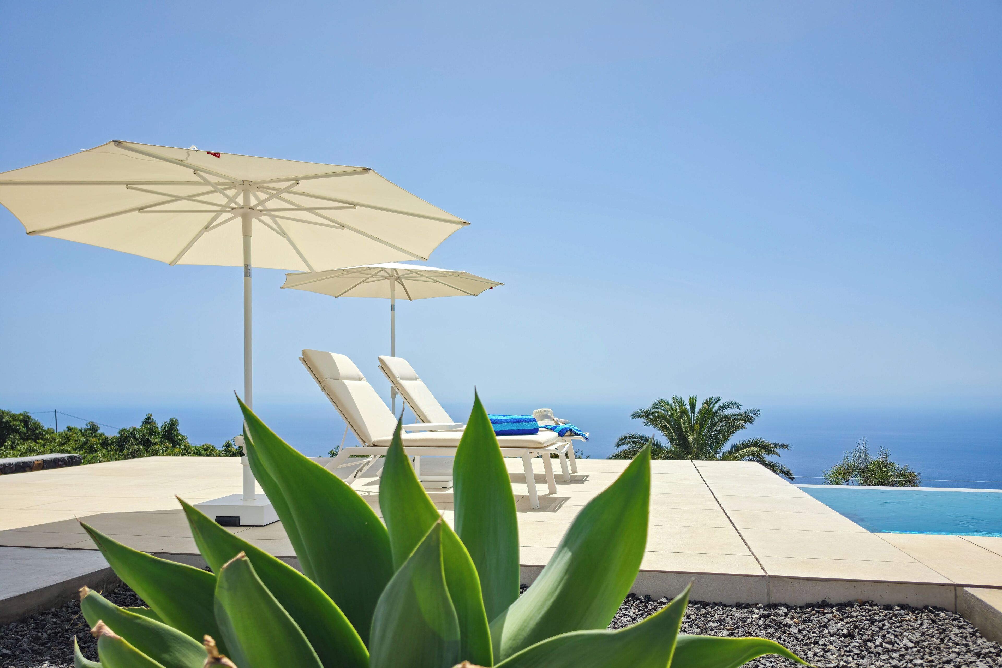 A poolside area with lounge chairs and umbrellas, overlooking a clear blue sky and ocean view.