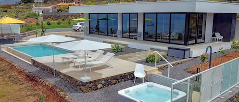 Ett modernt hus med en swimmingpool, utomhusmöbler och en bubbelpool.