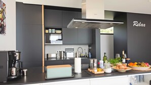 Een moderne keuken met een koffieapparaat, een broodtrommel en een schaal fruit op het aanrecht.
