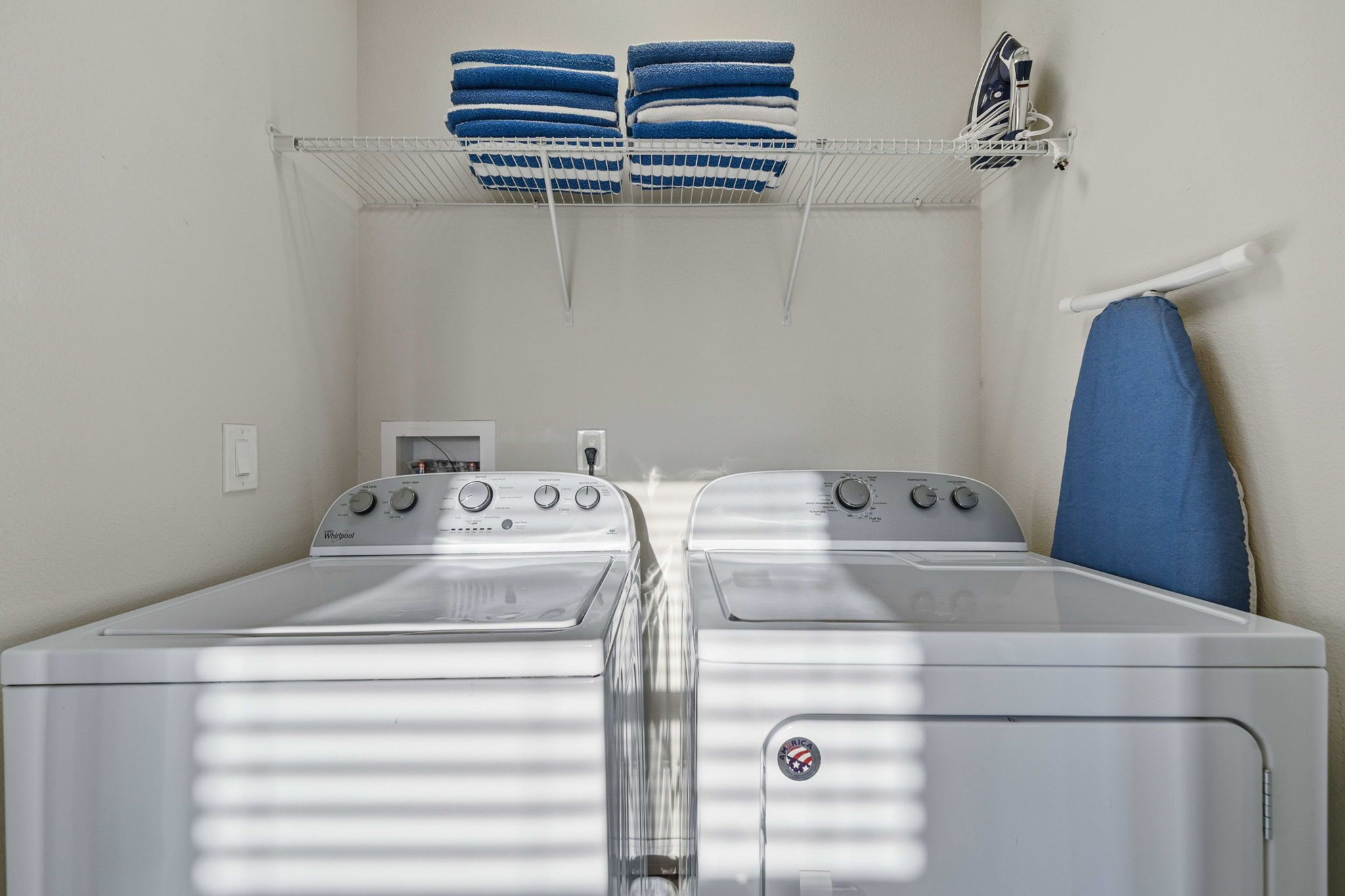 A laundry room with two front-loading washers, a drying rack with folded towels, and an ironing board.