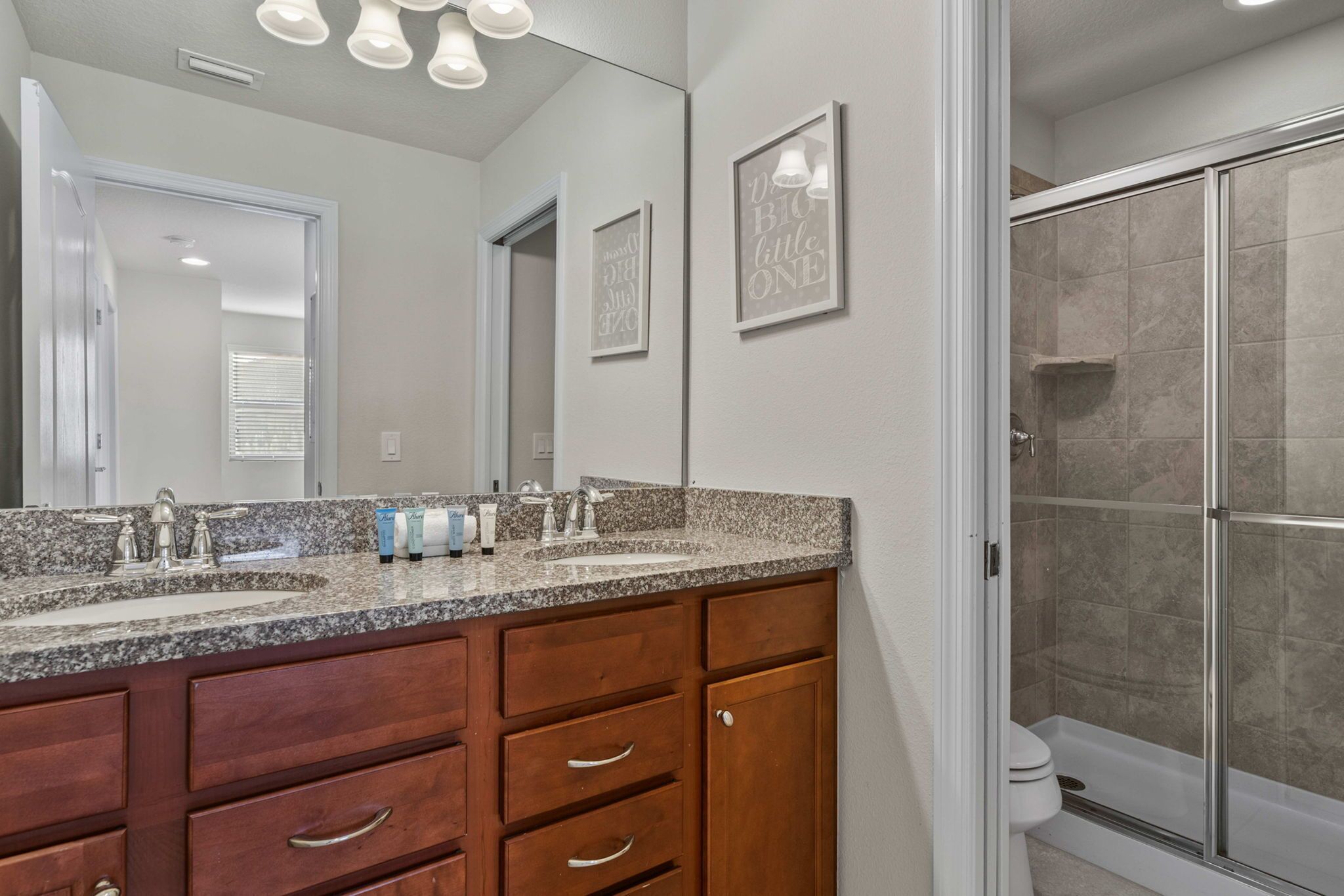 A bathroom with a double sink vanity, a glass shower enclosure, and a mirror with wall art.