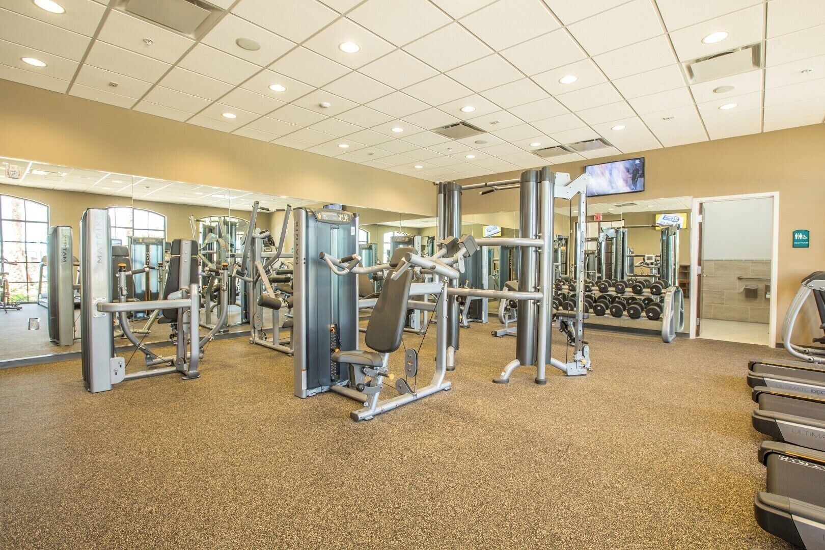 A gym with various exercise machines, a mirrored wall, and a television screen.