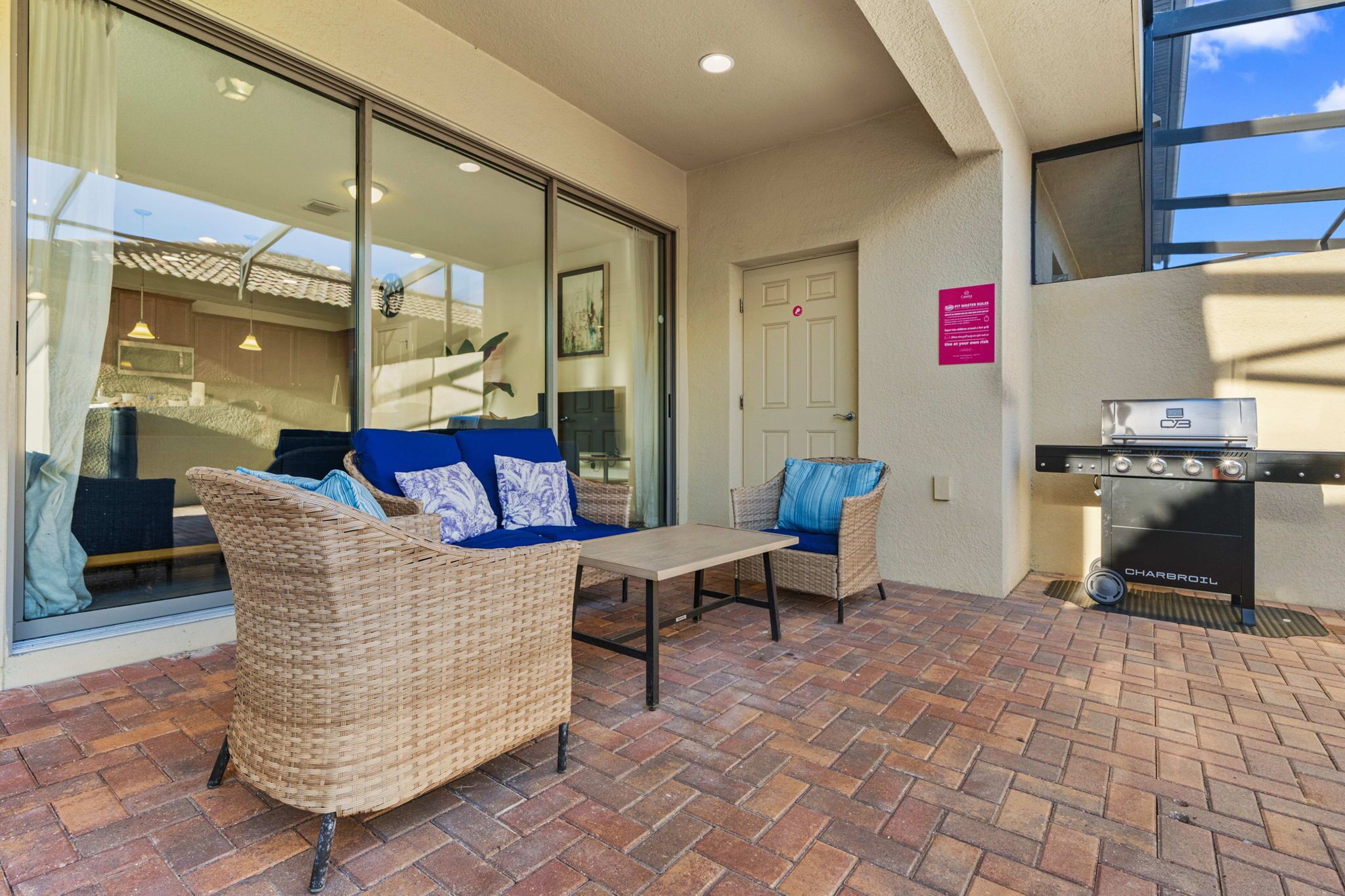 A patio area with wicker furniture, a charcoal grill, and a view of the interior.