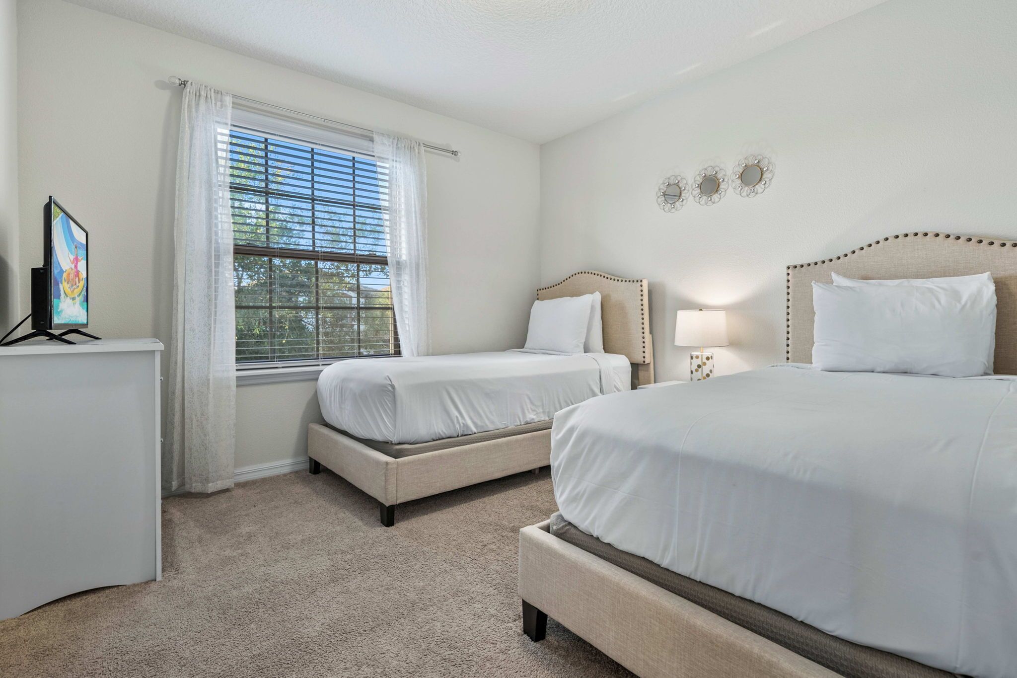 A bedroom with two beds, a desk, a window with curtains, and wall-mounted decor.