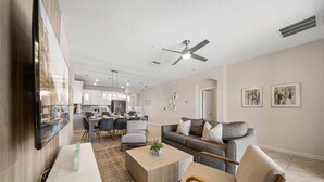 Ein modernes Wohnzimmer mit Sofa, Couchtisch und Fernseher. Im Hintergrund befindet sich eine Essecke mit Stühlen und eine Küche.