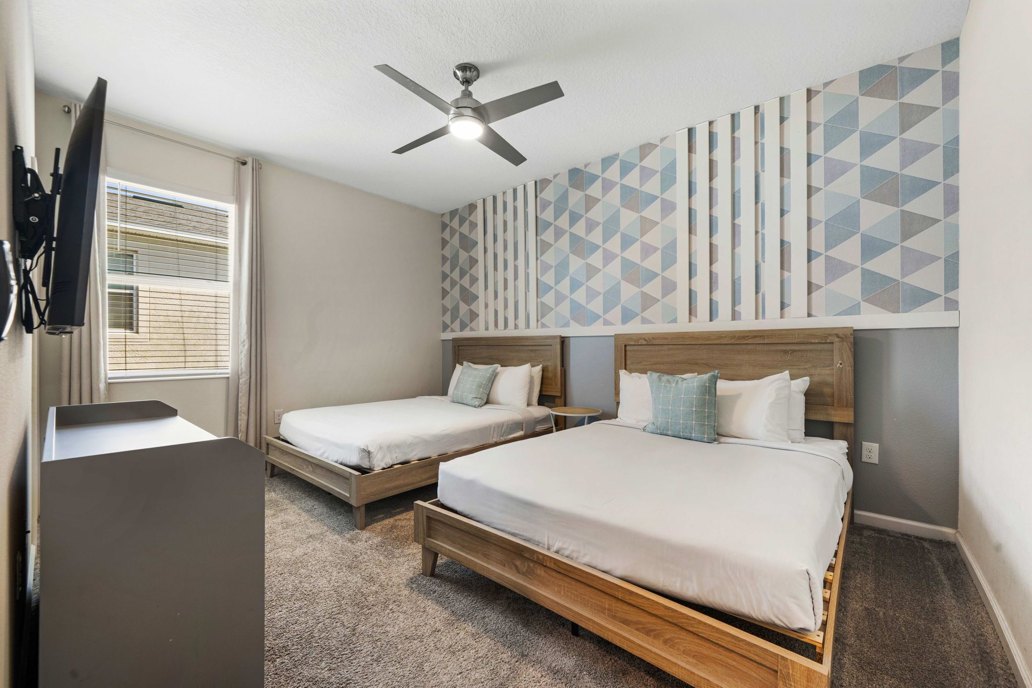 A bedroom with two beds, a ceiling fan, a TV, and a patterned wall.