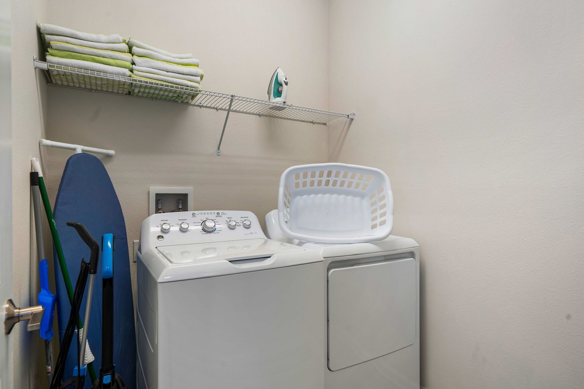Un espace dédié à la lessive, comprenant un lave-linge, un étendoir, un panier et des ustensiles de nettoyage.
