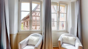 A room with two white armchairs, a large window with curtains, and a view of traditional buildings outside. - Les gîtes d'Elouise 2 (Colmar)