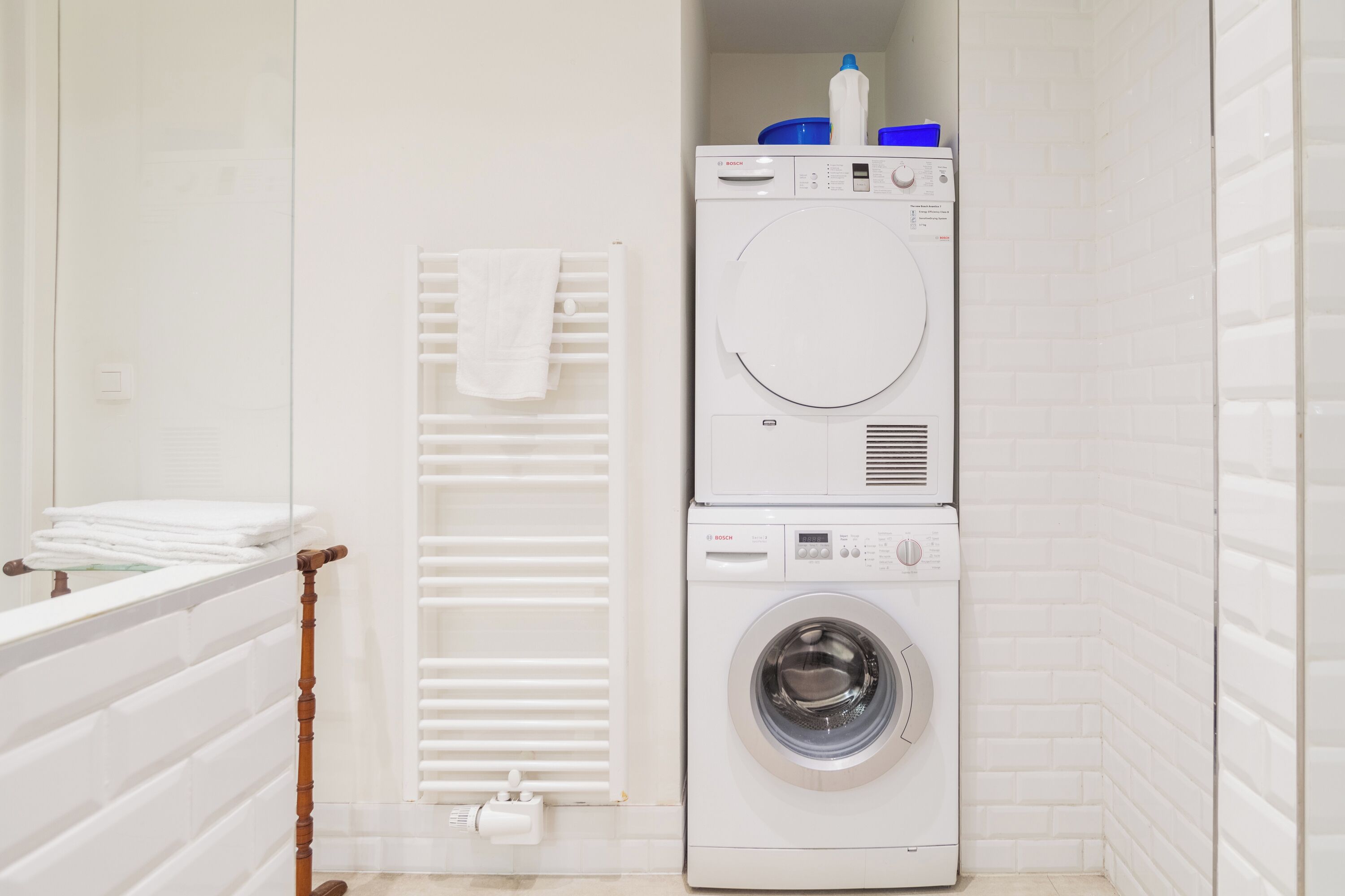 A compact laundry area with a stacked washer and dryer, a towel rack, and a radiator.