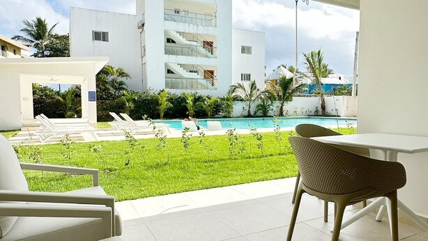 A modern hotel room with a balcony, a pool, and a view of a white building with multiple floors. - Beach Walk and Direct Pool Access (Cabarete)