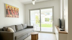 A modern living room with a grey sofa, a round wooden coffee table, a ceiling fan, and a TV on a wooden stand. - Beach Walk and Direct Pool Access (Cabarete)