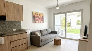 A modern living space with a kitchen, a grey sofa, a coffee table, and a sliding glass door to a balcony. - Beach Walk and Direct Pool Access (Cabarete)
