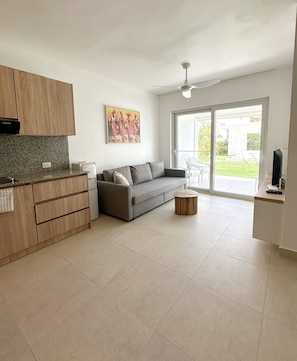 Ein stilvoller Wohnraum mit einer Küche, einem grauen Sofa, einem Couchtisch und einer Schiebetür zum Balkon.