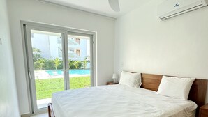 A bedroom with a bed, a ceiling fan, an air conditioning unit, and a view of a pool through a glass door. - Beach Walk and Direct Pool Access (Cabarete)