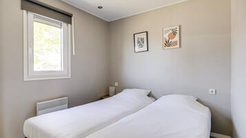 A room with two single beds, a window with a blind, a radiator, and two framed pictures on the wall.