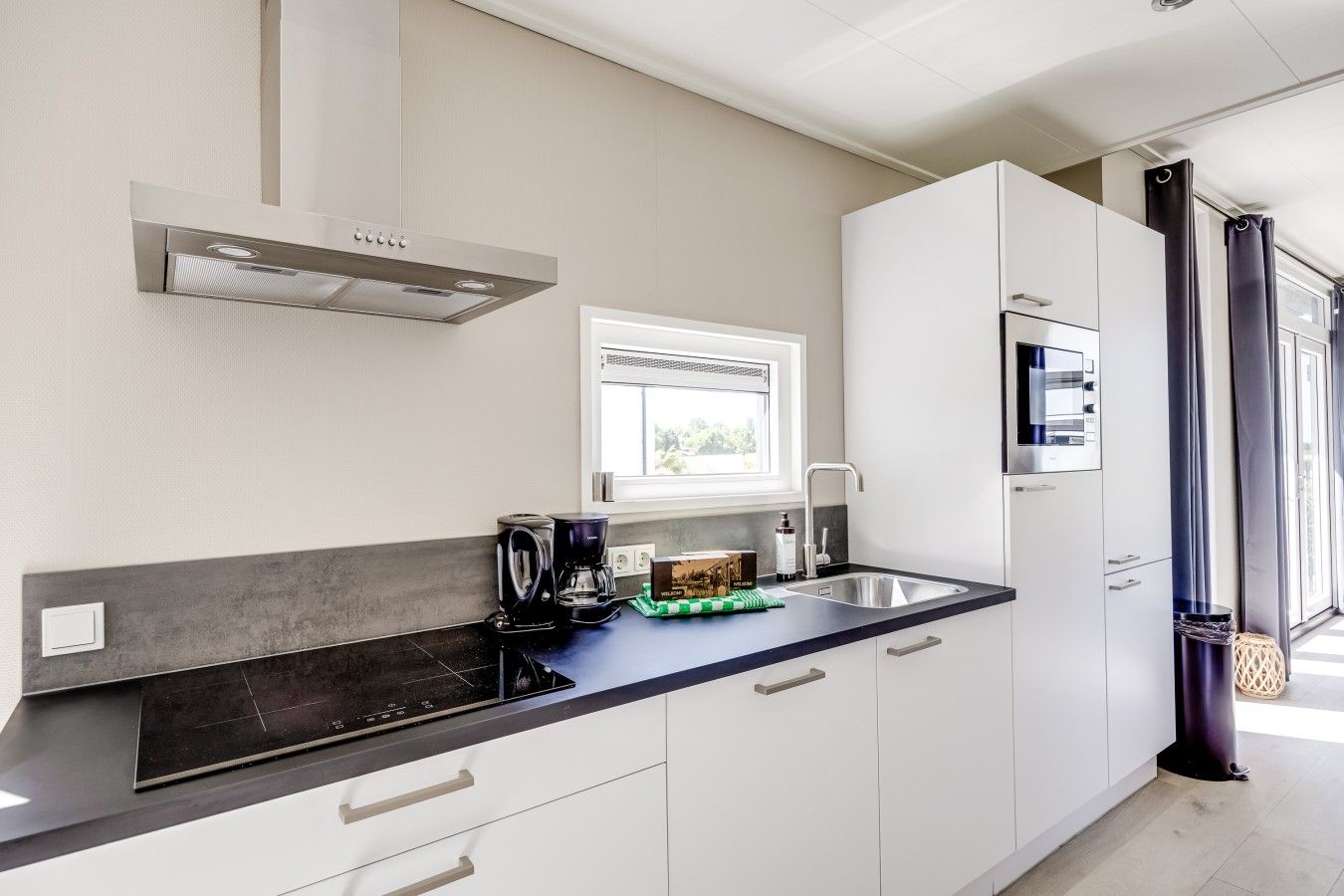 A modern kitchen with a built-in stove, a coffee maker, and a window above the sink.