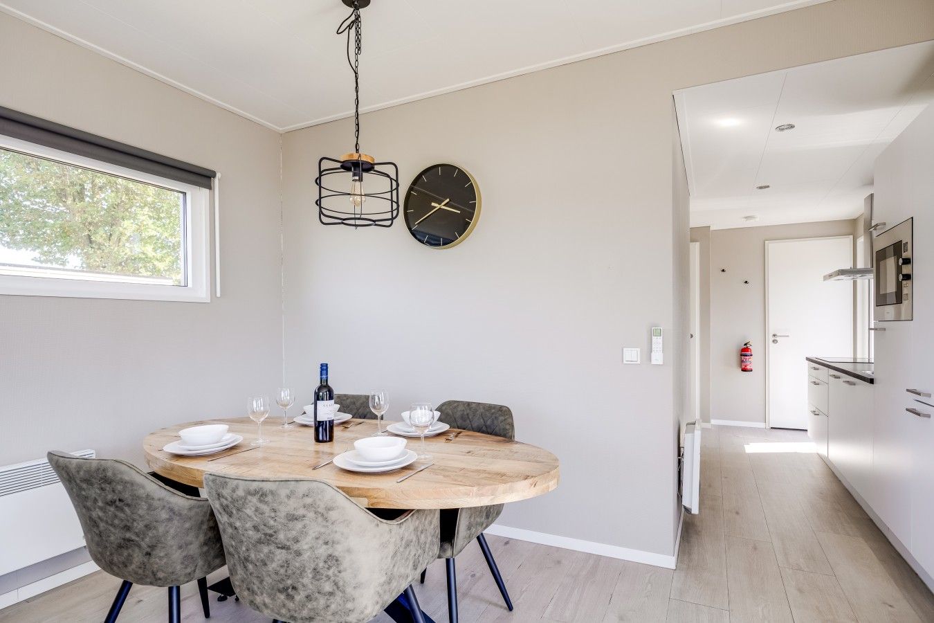 Un comedor moderno con una mesa redonda, sillas, una botella de vino y un reloj en la pared.