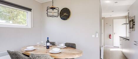 Un comedor moderno con una mesa redonda, sillas, una botella de vino y un reloj en la pared.
