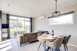 Un comedor moderno con una mesa redonda de madera, sillas tapizadas en gris y un televisor montado en la pared.