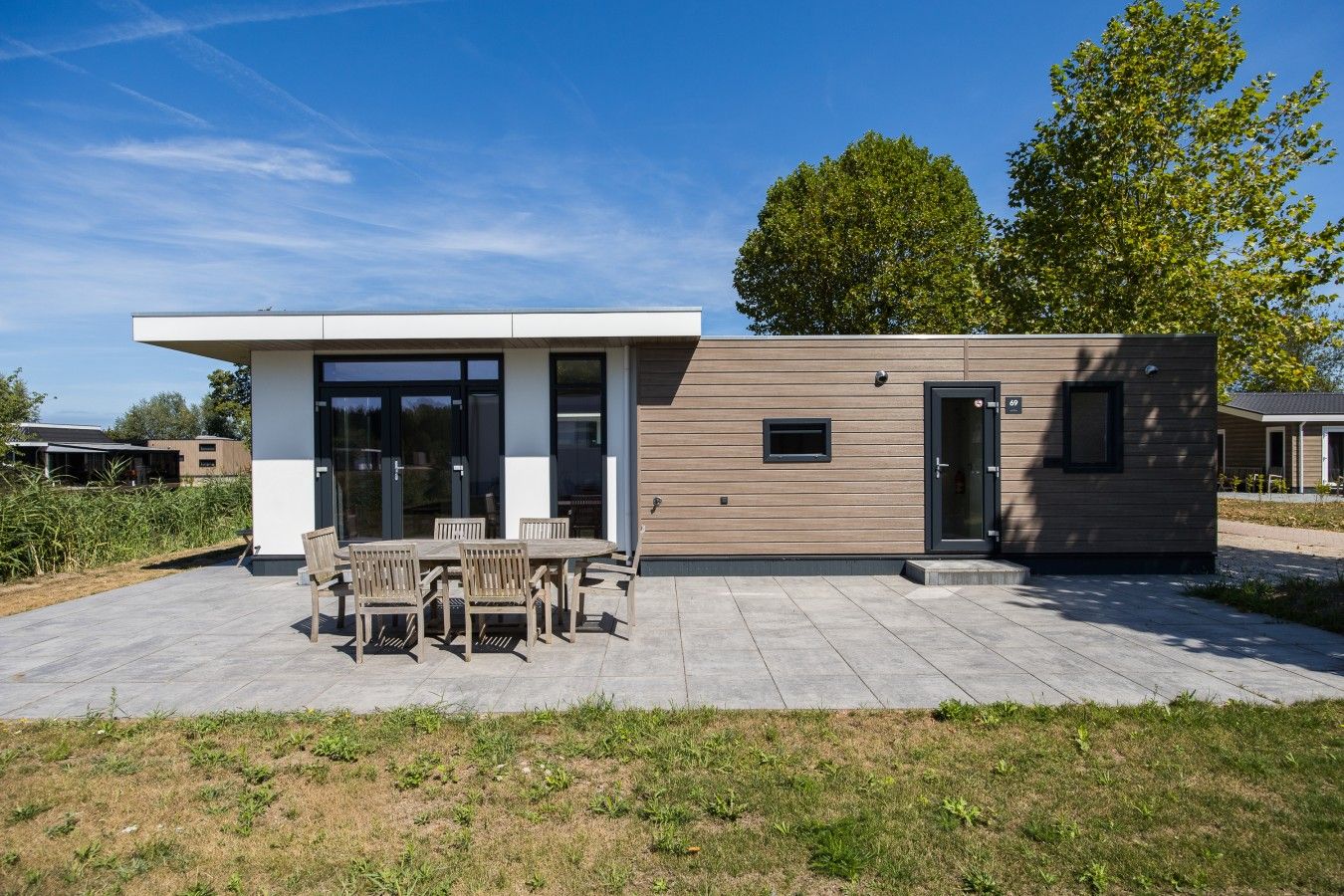 A modern house with a patio, a dining area with wooden furniture, and a small attached structure.