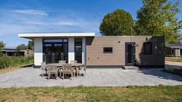 A modern house with a patio, a dining area with wooden furniture, and a small attached structure.