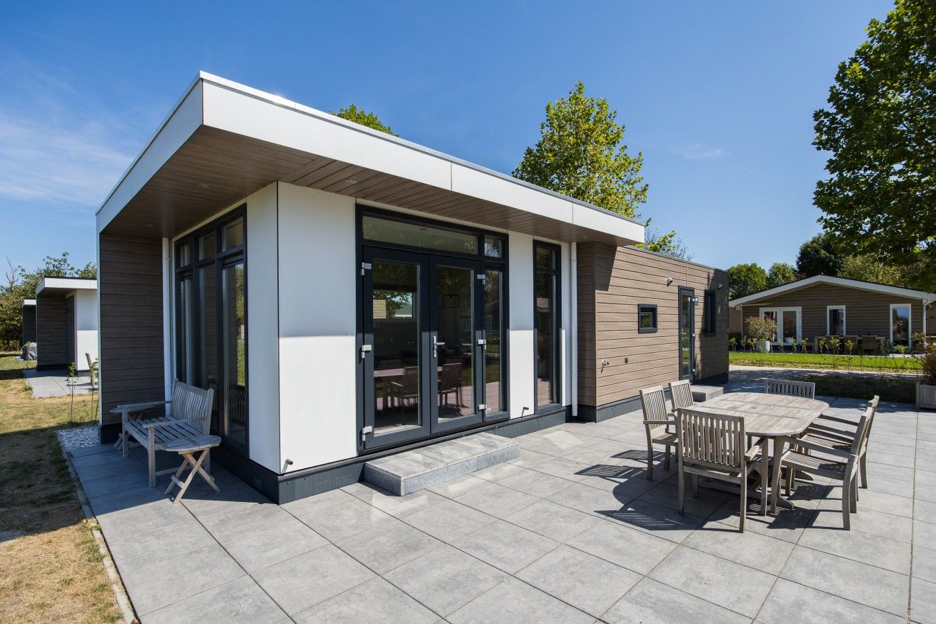 A modern outdoor patio area with a dining table and chairs, a bench, and a covered seating area.