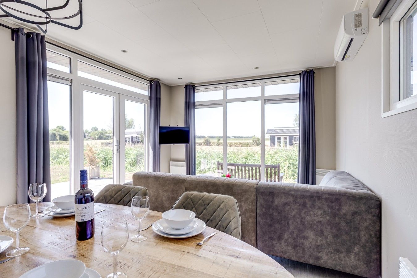 A dining area with a table set for two, a sofa, and a TV mounted on the wall.