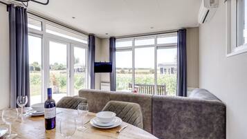 A dining area with a table set for two, a sofa, and a TV mounted on the wall.
