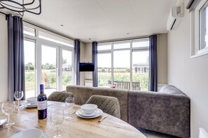 A dining area with a table set for two, a sofa, and a TV mounted on the wall. - Cube XL 69 | 4 persoons chalet in Zennewijnen (Zennewijnen)
