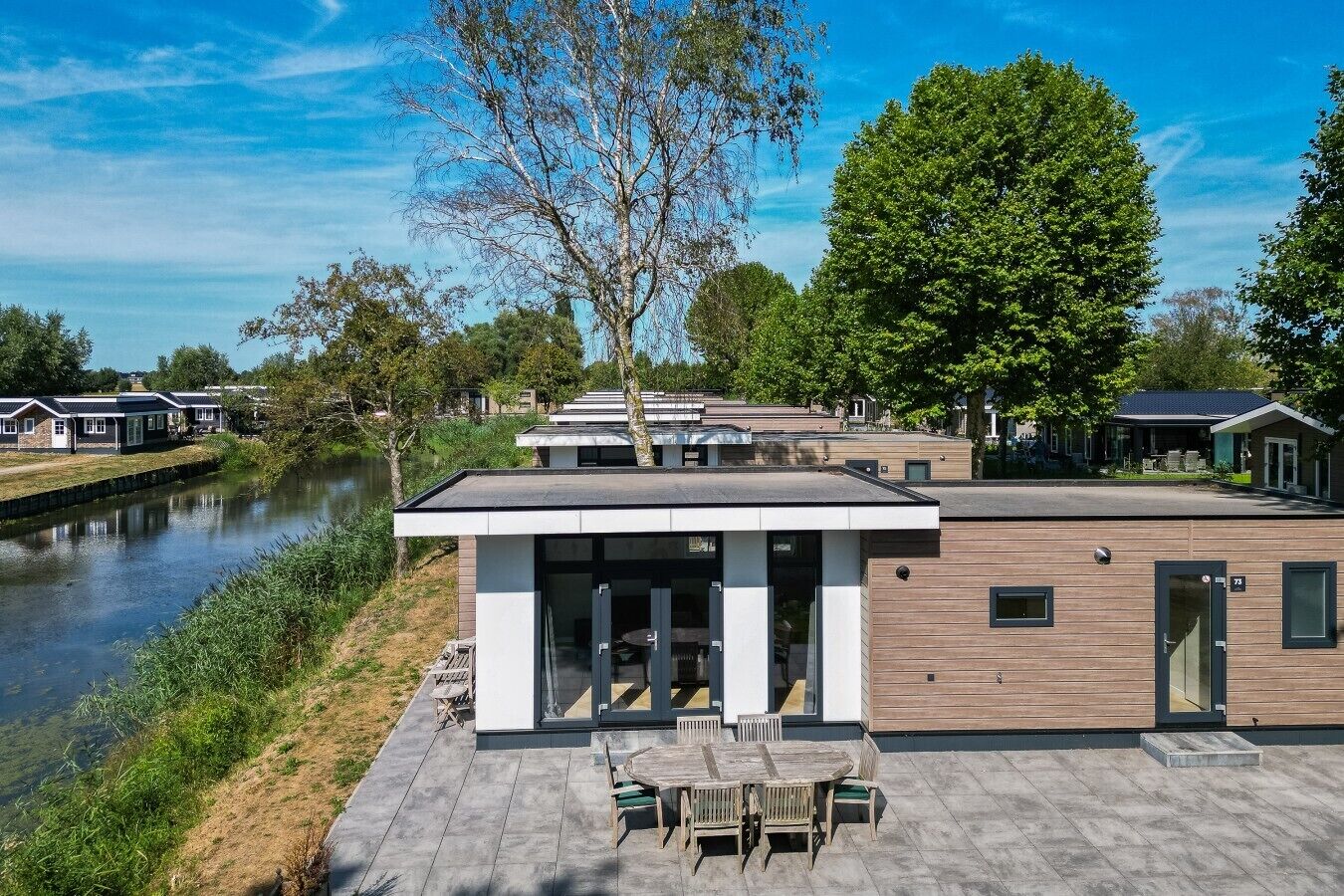 A modern building with a flat roof, large windows, and a patio area with outdoor furniture.