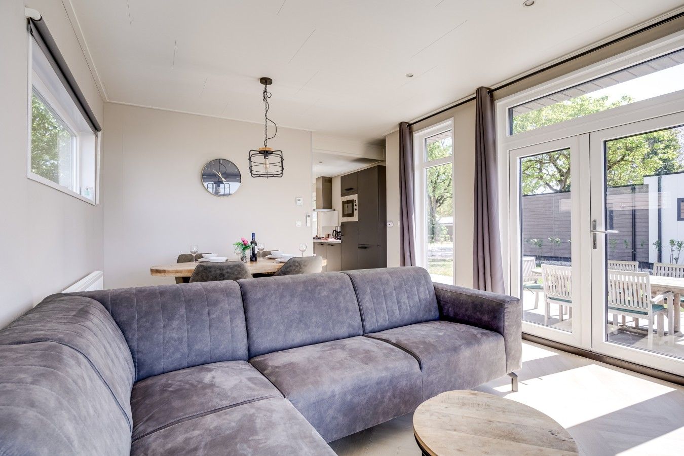 A modern living room with a grey sofa, a wooden coffee table, and a dining area with a table and chairs.