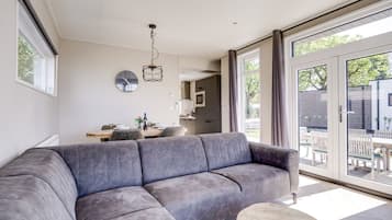 A modern living room with a grey sofa, a wooden coffee table, and a dining area with a table and chairs.