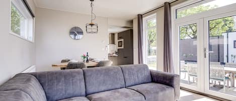 Een moderne woonkamer met een grijze bank, een houten salontafel, en een eethoek met een tafel en stoelen.