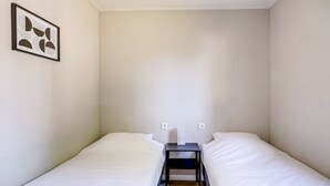 Un alojamiento pequeño y con una sola habitación, con dos camas, una mesita y un interruptor de luz en la pared.