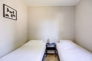 Un alojamiento pequeño y con una sola habitación, con dos camas, una mesita y un interruptor de luz en la pared.