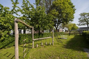 Ein Spielplatz mit Holz-Klettergerüsten und Schaukeln, umgeben von üppigem Grün und Bäumen.
