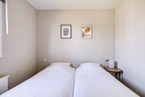 A hotel room with two beds, a small bedside table with a lamp, and two framed pictures on the wall.