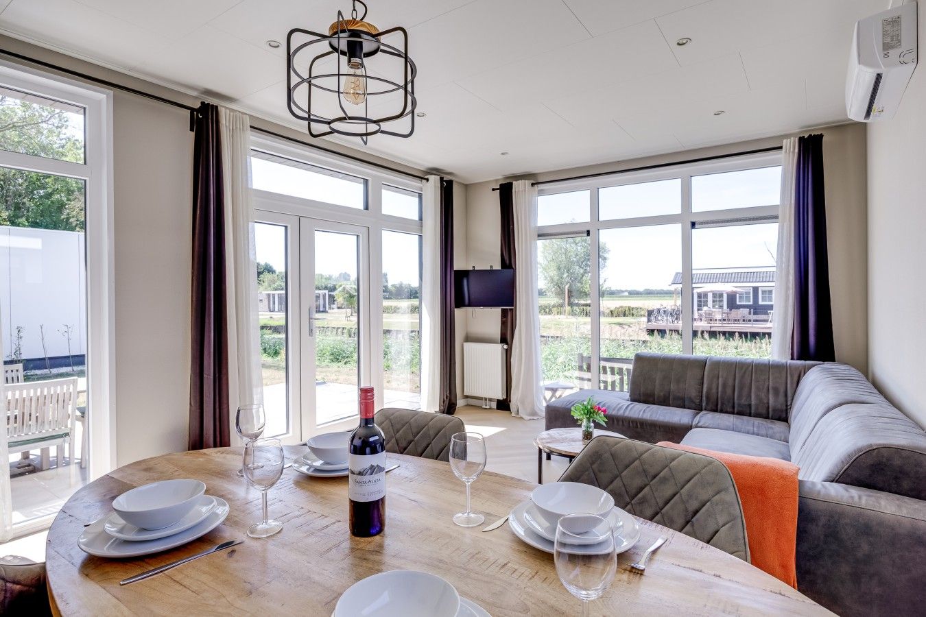 A dining area with a wooden table set for two, a bottle of wine, and a television on the wall.