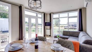 A dining area with a wooden table set for two, a bottle of wine, and a television on the wall.