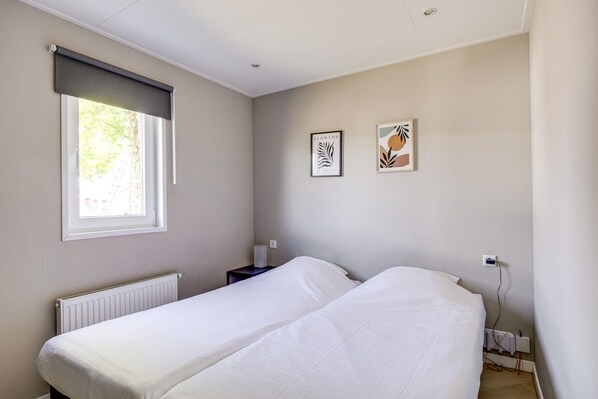 Un dormitorio con dos camas, un radiador, una ventana con persiana y dos cuadros en la pared.